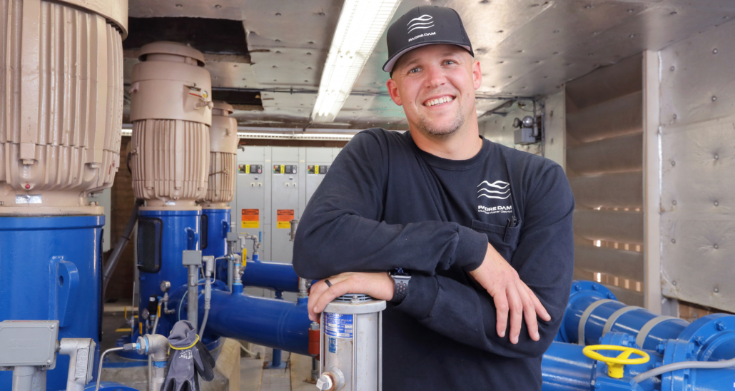 Smiling technician standing confidently inside a modern water treatment or industrial facility.

