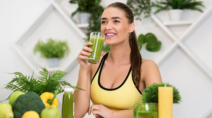 "Fit woman in activewear enjoying a green detox drink post-workout, surrounded by fresh fruits and plants — representing how sweating and staying hydrated with On Take Water aids in natural detoxification through perspiration."