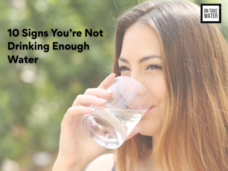 Woman drinking a glass of water with text overlay "10 Signs You’re Not Drinking Enough Water" and On Take Water logo in the top right corner.