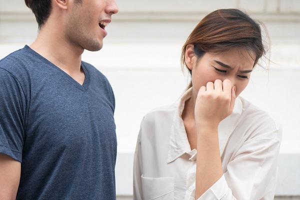 A woman covering her nose in discomfort while standing near a man, indicating bad breath caused by dry mouth — a common sign of dehydration. Staying hydrated with On Take Water can help combat dry mouth and promote fresh breath naturally.
