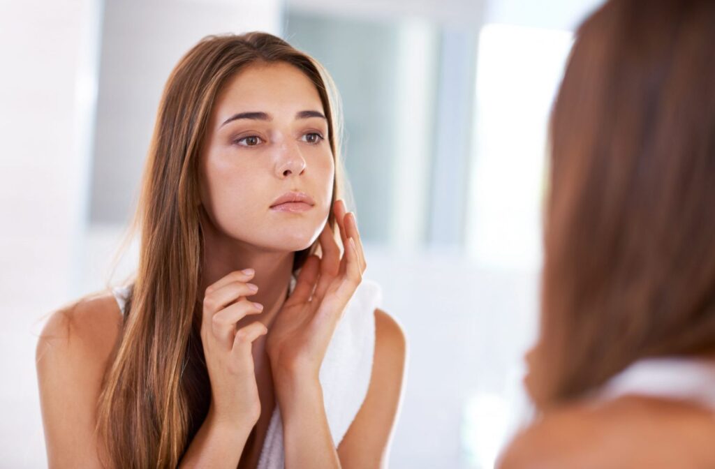 "Young woman examining her face in the mirror, noticing reduced puffiness and inflammation after regular hydration with On Take Water – promoting clearer and healthier skin."