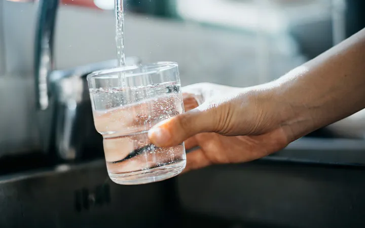 A close-up of a hand holding a glass under a faucet as water is being filled into it. 