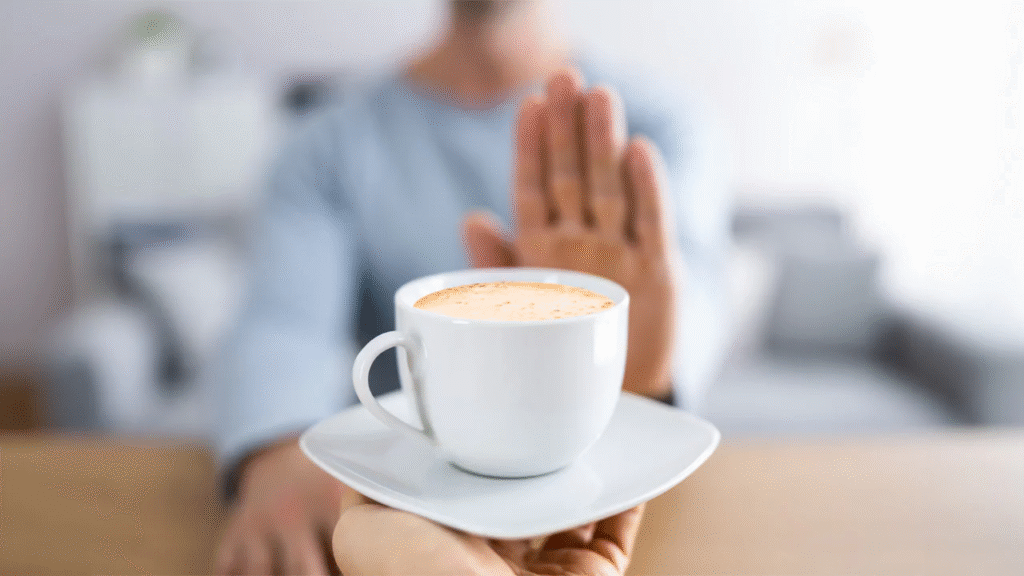 Person in a light blue shirt raising a hand to refuse a cup of coffee, symbolizing the negative effects of caffeine, such as anxiety, insomnia, and dependence.
