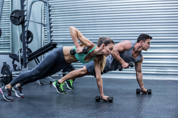 Fit man and woman in athletic wear performing plank rows with dumbbells in a gym, representing enhanced performance and stamina by combining water and caffeine wisely during workouts.