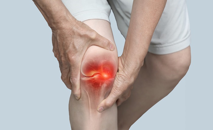 A person holding their knee in pain, with a highlighted red area around the knee joint indicating inflammation or joint pain.